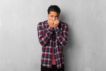 Man over grunge wall is a little bit nervous and scared putting hands to mouth