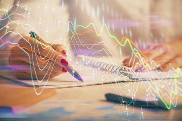 Double exposure of woman's hands making notes with forex graph hologram. Concept technical analysis.