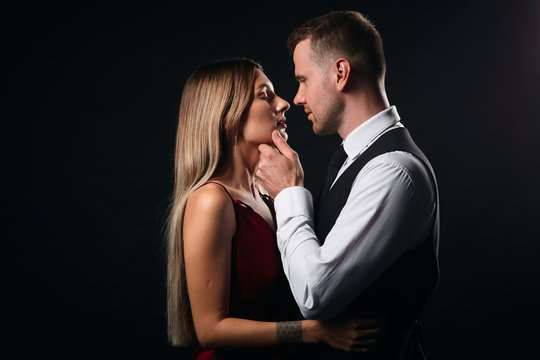 awesome young stylish giving warm, deep kiss to a lady in red dress, close up side view photo. isolated blackbackground, studio shot.