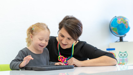 Toddler girl in child occupational therapy session doing playful exercises on a digital tablet with her therapist.