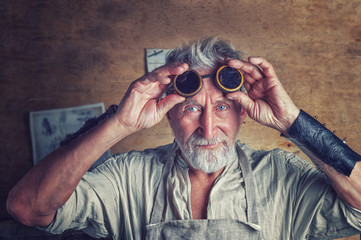 Gray-haired bearded man in steampunk glasses, fantasy, fairy tale. Inventor in  post apocaliptic world