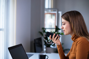Young woman recording audio message on the phone at the office