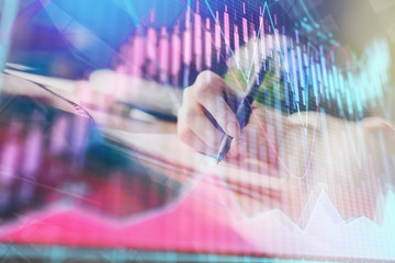 Financial forex graph displayed on hands taking notes background. Concept of research. Multi exposure