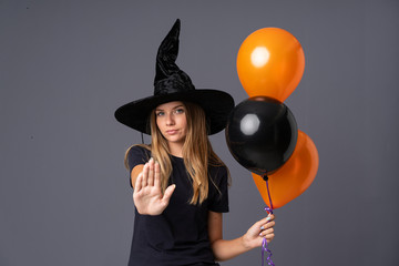 Young witch holding black and orange air balloons making stop gesture with her hand