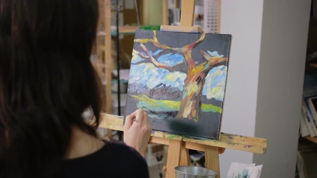 Woman is depicting landscape on canvas in art therapy class, view from back
