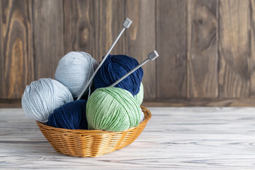 Knitting blue and green yarn in a basket with needles on wooden background