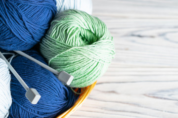 Knitting hobby composition with blue and green yarn and needles on white wooden background.