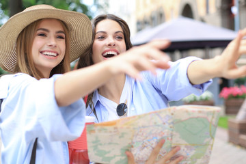 Holidays and tourism concept - beautiful girls looking for direction in the city.