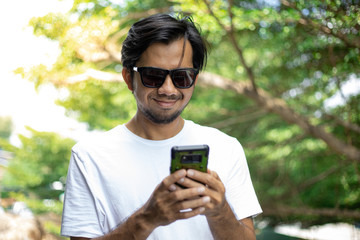 Young asian man wear sunglasses and enjoying smartphone outdoors