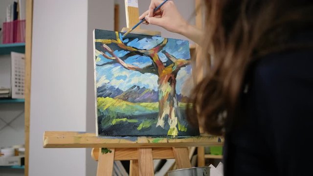 Brunette woman is drawing sky on abstract picture in art-therapy class, closeup