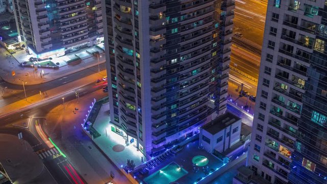 View of towers with swimming pool and traffic on intersection in Dubai Marina from above aerial night timelapse. Illuminated modern buildings in urban skyline