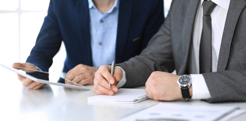 Two unknown businessmen or partners using tablet pc and discussing questions at meeting in modern office, close-up of hands. Group of managers at negotiation or brainstorm. Teamwork, partnership and