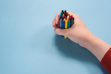 Bunch of wax colorful pencils in female hand on blue background.