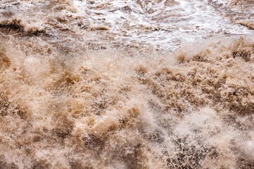 Obraz premium Waves of muddy water crash into each other in the rapids in a gorge creating splashes and a myriad of droplets in an astonishing display of nature forces and power