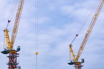 Photo of two industrial cranes with background of sky and cloud. Concept of building site, construction business, engineering, heavy lift machinery.