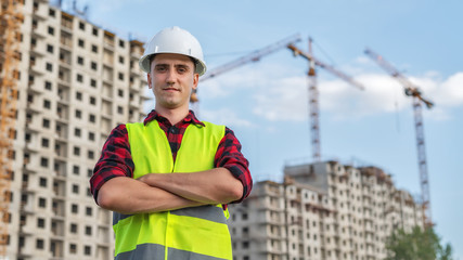 civil engineer in white helmets and a yellow vest on the background of the house under construction.