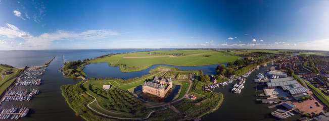 Wide aerial panoramic view of the Muiderslot castle in Muiden near Amsterdam and its lush gardens at the IJsselmeer with surrounding water entrenchment and port area and harbour of the historic city