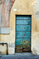 Close-up of an old green painted door on a scraped wall with an ancient brick arch, Lucca, Tuscany, Italy 