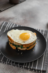 delicious breakfast sandwich with fried egg, spinach and cheese on a dark plate. close-up
