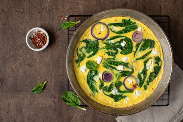 omelet with spinach and feta cheese in an iron pan on a wooden, rustic background. Top view. copy space
