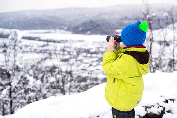 Happy spy boy looking for Santa claus with christmas gifts in a mountains. Winter family vacation, travel, holidays.