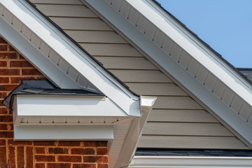 Gable with brick and vinyl siding, white frame gutter guard system, fascia, drip edge, soffit, on a pitched roof attic at a luxury American single family home neighborhood USA © tamas