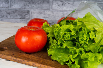 Red tomatoes with water droplets and green lettuce are on a wooden board.