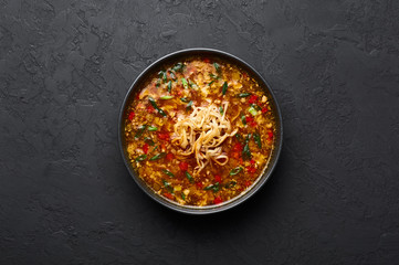 Veg Manchow Soup in black bowl at dark slate background. Vegetarian Manchow Soup is indo-chinese cuisine dish with bell peppers, cabbage, carrot, noodles, chilli, soy sauce and green onion.