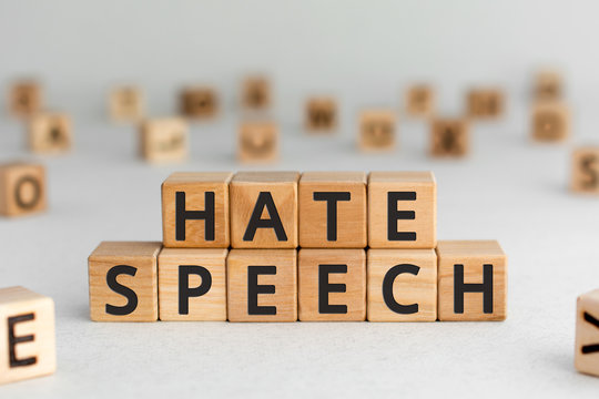 Hate speech - words from wooden blocks with letters, speech that attacks a basis attributes such as race, religion, gender identity hate speech concept, random letters around, white  background