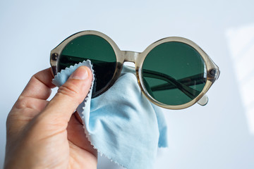 Woman's left hand cleaning sunglasses by microfibre cleaning cloths, On white background, Close up...