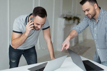 Fototapeta premium Portrait of two self-confident businessman working at laptop. One man talking on smartphone when another guy pointing with finger on screen.