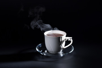 White cup in the dark with a hot drink and steam above it