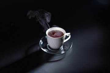White cup in the dark with a hot drink and steam above it