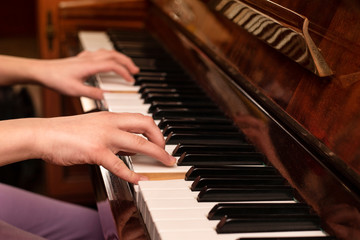 Obraz na płótnie Canvas A young teenage girl playing at home on the piano, her hands gracefully playing a familiar tune. Music education helps the girl to develop