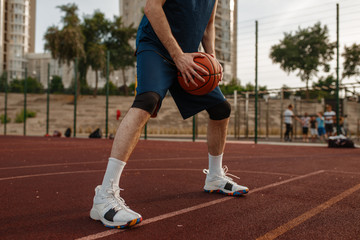 Obraz premium Male basketball player holds a ball, outdoor court