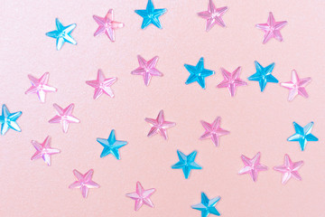 Festive flat lay: pink and blue rhinestones in the form of stars on a pastel pearl pink background. Minimalism, top view, design, monochrome.