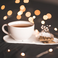 Cup of green tea with matcha chocolate and floers on tray over lights. Good morning. Breakfast.