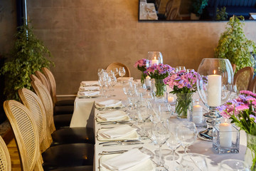Table setting for guests in a restaurant, on the table forks and glasses for wine - flowers in a vase and a candle on the table