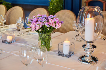 Table setting for guests in a restaurant, on the table forks and glasses for wine - flowers in a vase and a candle on the table