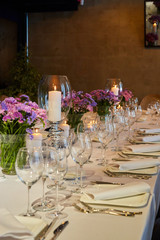 Table setting for guests in a restaurant, on the table forks and glasses for wine - flowers in a vase and a candle on the table