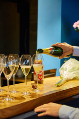 Glasses of wine stand on a wooden bar - waiter's hands pour champagne into a glass