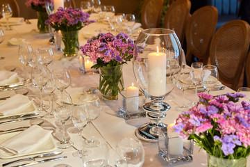 Table setting for guests in a restaurant, on the table forks and glasses for wine - flowers in a vase and a candle on the table