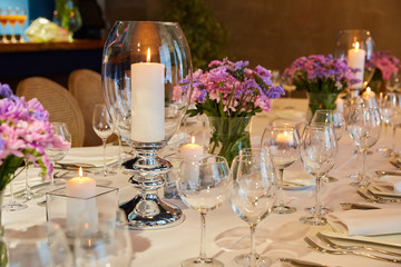 Table setting for guests in a restaurant, on the table forks and glasses for wine - flowers in a vase and a candle on the table