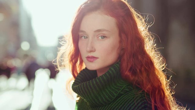 shot on Arra Alexa Mini beautiful dreaming young woman with spectacular curly red ginger hair looking at camera posing outdoor in downtown street. Female portrait.