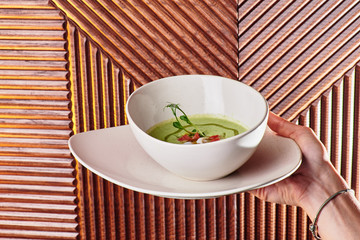 Woman holds a plate with Green cream spinach soup decorated with tomatoes and mushrooms. Dark textured background. Close-up. Space