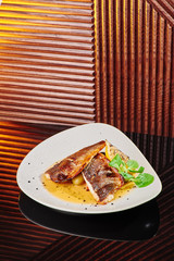 White steak of grilled fish on pillow of vegetables and yellow sauce, with lemon slice and fresh herbs. Fish on white plate on dark beautiful background. Close-up. Space