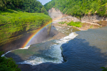 Fototapeta na wymiar A rainbow forms at the top of a waterfall at Letchworth State Park in New York State on a sunny day in summer. 