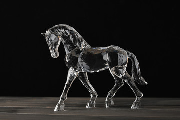 Crystal horse in drops of dew on a wooden shelf