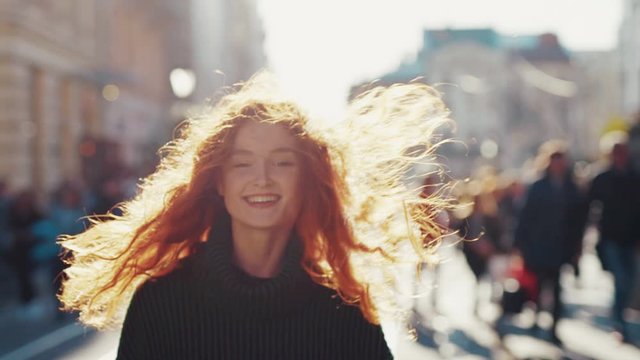 Amazing portrait of spectacular smiling redhead young woman walking backward in crowded street exploring city center in sunny weather.
