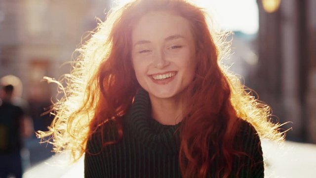 Outdoor portrait of attractive caucasian model with curly ginger hair adorable smile enjoying walk in city center. Beauty and femininity concept.